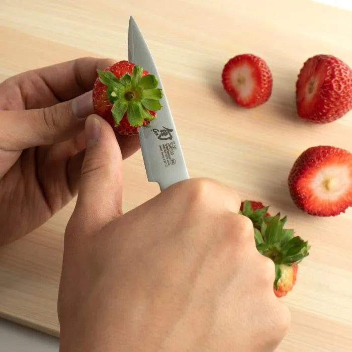 Person cutting a strawberry with a Shun Classic knife on a wooden surface
